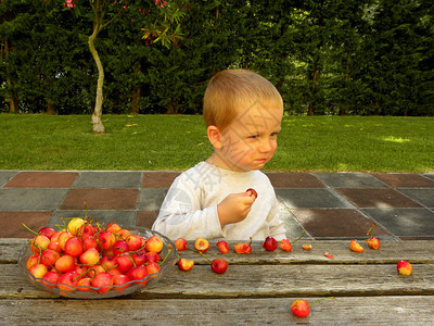 迷人的金发男孩坐在木桌边吃红樱桃三岁男孩吃甜图片