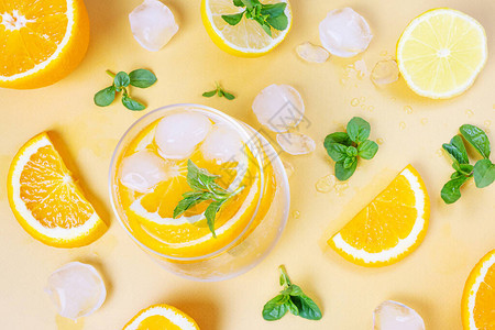 深色背景透明玻璃杯中的橙色冷鸡尾酒周围新鲜橙片冰块和薄荷片顶视图图片