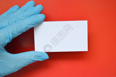 蓝橡胶手套上的一只手拿着一张红色背景的白纸图片