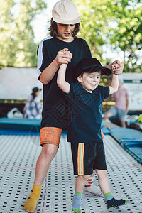 白种人儿童在蹦床上一起跳两兄弟手牵在蹦床上玩得很开心孩子们在户外蹦床上跳跃童年的友谊图片