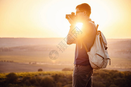 带背包和照相机的摄影师拍摄日落山脉照片的男摄影师旅行业余爱好概念冒险在图片