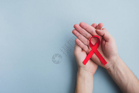 人手握着红色丝带感知Aids在浅蓝色背景上医学概念图片