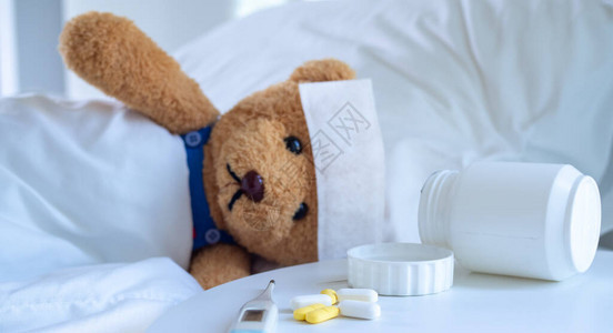 泰迪熊和退烧贴躺在一张白色床上的床上图片