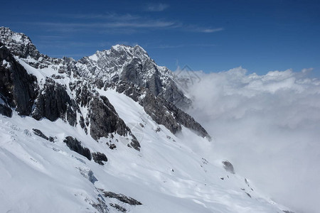 云南省玉龙雪山白雪坡壮丽的灰色山脉岩石被宽阔的白雪覆盖湛蓝的天空图片