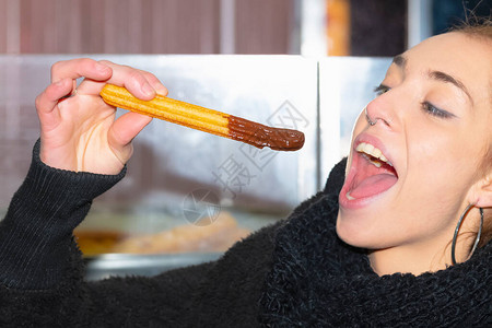 关闭一个年轻女子要咬一个美味的油条蘸巧克力在焦外的背景上美味图片