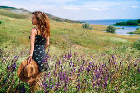 一个穿着裙子的快乐年轻女子戴着帽子在山丘地区盛开的野花和高草背图片