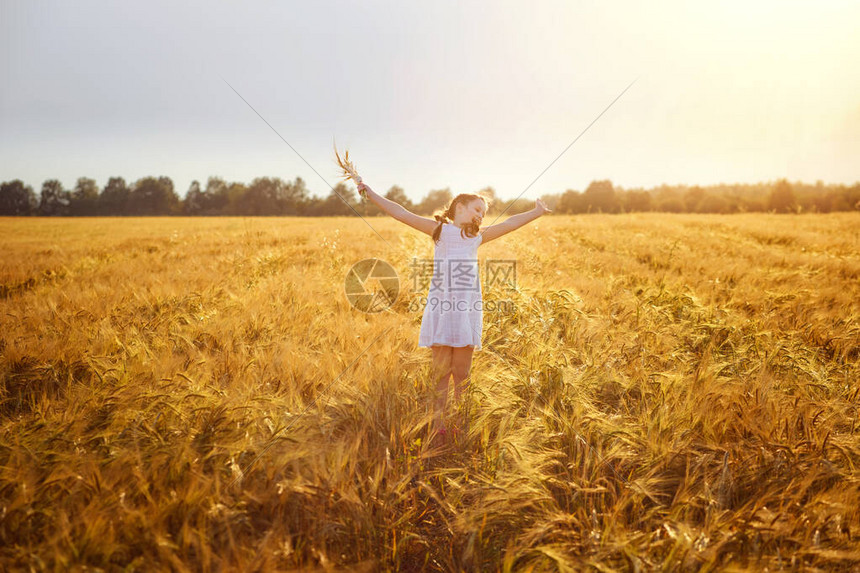 一个穿着白色吊带裙的快乐女孩在落日的光芒下跳上成熟的麦田麦穗黑麦的选择性焦点变得晴朗穿图片