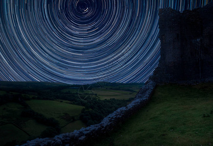 北极星周围星迹的数字合成图像与喜怒无常的天空背景中世纪城堡遗图片