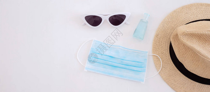 医疗面罩手凝胶清洁剂太阳眼镜和白床上的沙帽图片
