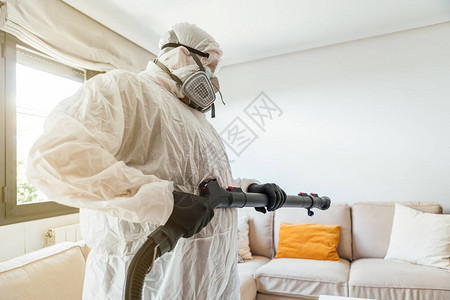 穿着PPE的男子用COVID19消毒机对房子的客厅进行消毒大流行背景图片