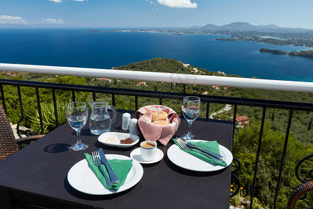 在俯瞰希腊科孚岛海岸的餐厅露台上为两人准备的餐桌在桌上的咖啡水和图片