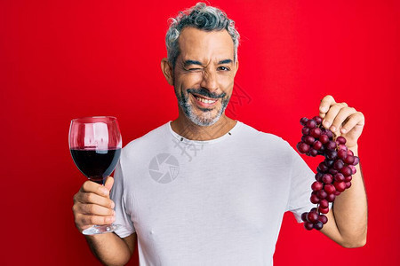 中年灰色头发男子拿着新鲜葡萄和红酒的枝子图片