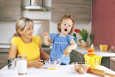 一位母亲和她的小女儿正在准备烘焙原料桌子上有鸡蛋牛奶面粉和擀面杖一个小女孩用打蛋器打鸡蛋家庭度假背景图片