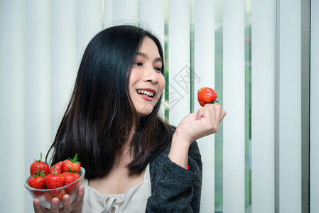亚洲美貌女持有并吃新鲜草莓是红莓果色和甜的多汁图片