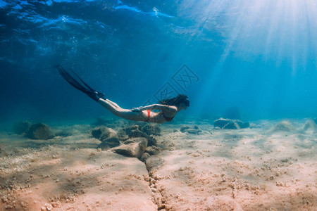 蓝海和太阳光线中比基尼滑翔的白自由潜水的瘦女人图片