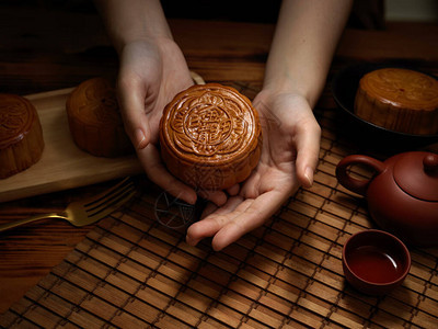关闭了女手拿着月饼在中秋节餐桌设置上方的视图月饼上的汉字用英文代表图片