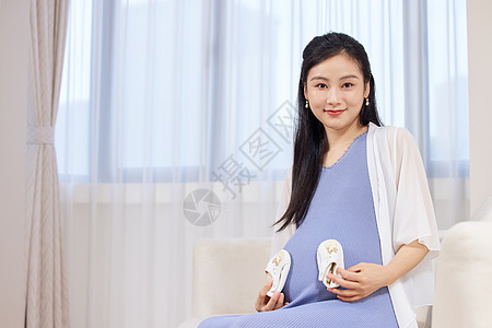 年轻居家孕妇手拿婴儿鞋图片
