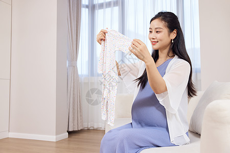 年轻居家孕妇手拿婴儿服装高清图片