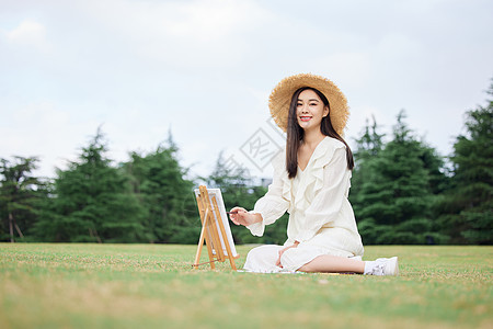 青年女性坐在草坪上绘画背景图片