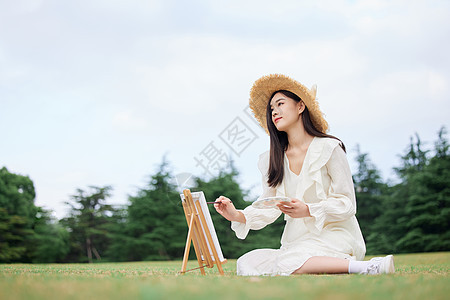 坐在草坪上绘画的青年女性背景图片