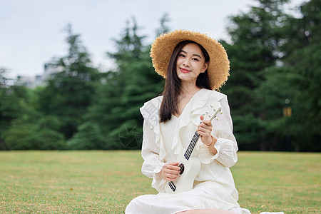 女孩谈尤克里里草坪上谈尤克里里的年轻美女背景