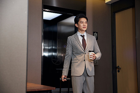 商务男士走出酒店电梯手拿咖啡图片