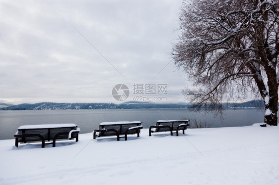 三个黑色的金属板凳被雪覆盖在湖边和山上图片