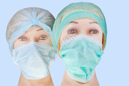 两名女假医生头戴纺织手术帽和蓝色背景隔离的图片