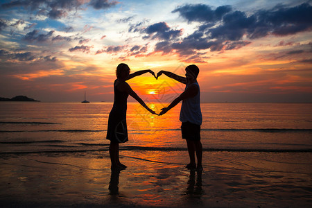 夕阳下海边牵手心形的情侣图片