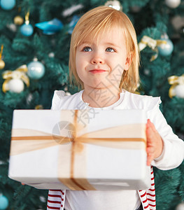 可爱的小女孩在圣诞树下拿着圣诞礼物图片