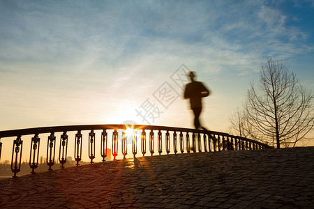 日出时跑过桥的慢跑者图片