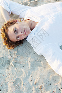 一个年轻的波西米亚男子的头部肖像日落时躺在金沙滩上深思熟虑图片