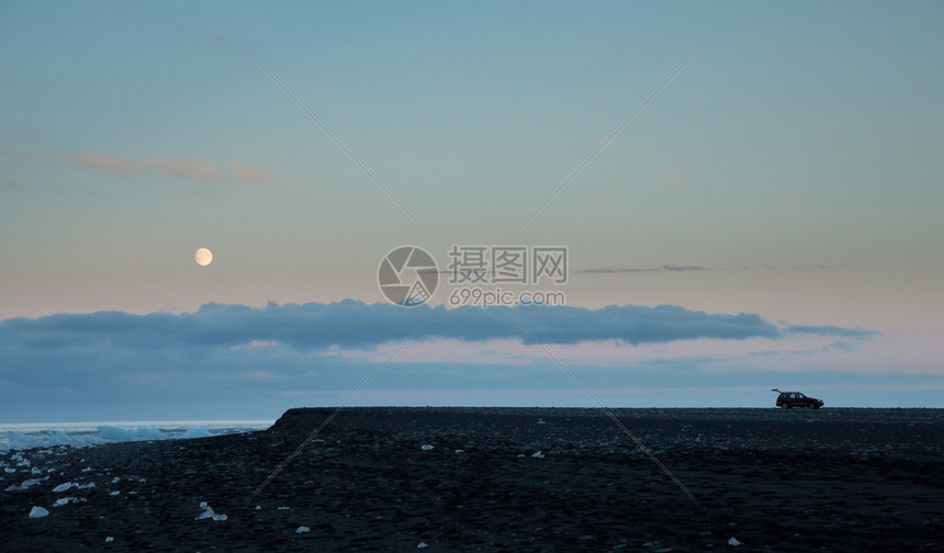 在日落时满月的Jokulsarlon海滩上长镜头长的旅游汽图片
