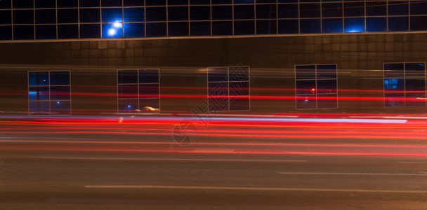 夜晚灯汽车在夜间穿过反射大楼时创造明亮的红色灯光小路背景