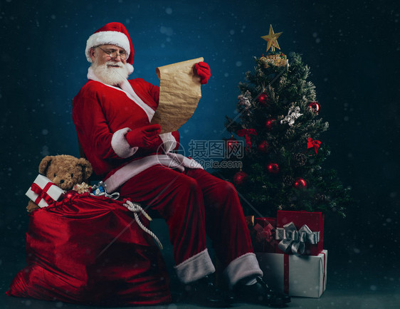 圣诞老人坐在圣诞礼物的堆叠上阅读愿望列表图片