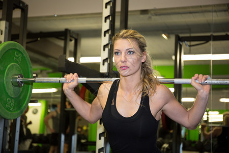 强壮的女人举杠铃作为运动量来找到锻炼程序的一部分适合在健身房举图片