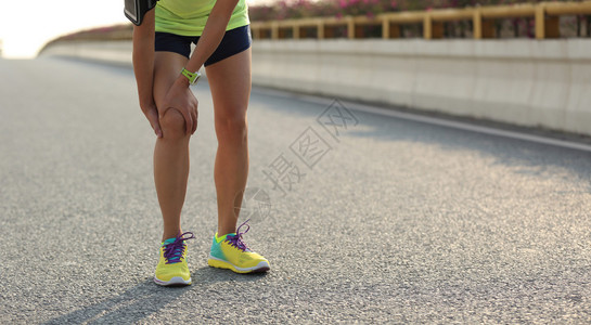 女子跑步者在路上抱着受伤的腿图片