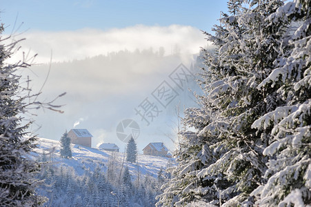 几座房屋坐落在覆盖着雪的山坡上背景中有蓝天云雾山从烟囱冒出的烟冬天阳光明媚图片