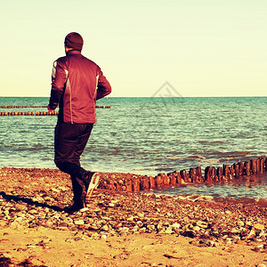 高个子穿着深色运动鞋在防波堤的石滩上跑步和锻炼生图片