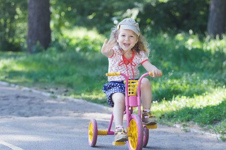 两岁的笑女孩戴着灯芯绒平帽和圆点服装骑自行车的孩子粉色背景图片