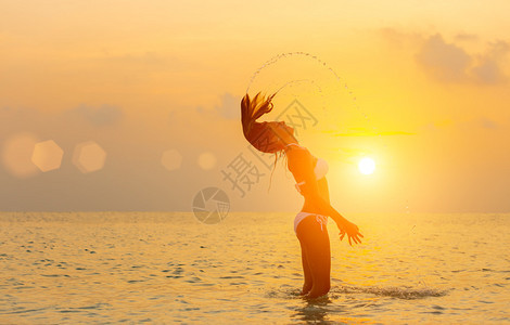 日落时在沙滩上跳跃的女孩四处溅水图片