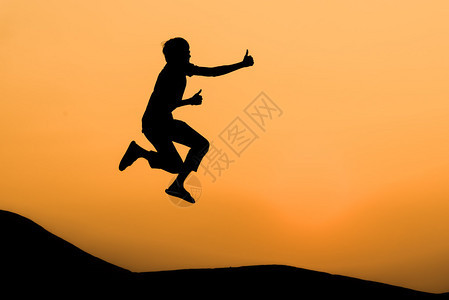 男人在欢快的跳跃中在橙色日落天图片
