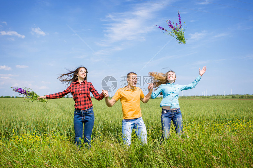 年轻的快乐朋友在绿色小麦田上奔跑一个男人和两个女孩跳起图片