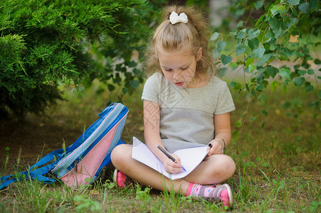 小学的女学生盘腿坐在树下做作业少女的眼神若有所思她的书包躺在女孩旁图片