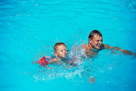 快乐的男孩享受与父亲一起游泳和溅水的乐趣幸福的家庭在游泳池的大海中玩耍孩子学游泳暑假概念爸和儿子在游背景图片