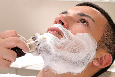 用剃刀和剃须肥皂在一个年轻男孩的理图片