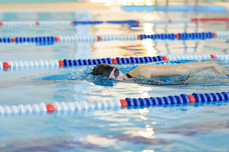 种红薯身穿护目镜和帽子在前排游泳的年轻女子在蓝水室内种背景