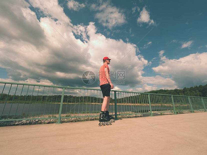 身穿红色t恤和黑色裤子的直排轮滑员在桥上滑冰的后视图在湖桥上光滑的混凝土地面上进行户外直排轮滑穿四轮靴图片