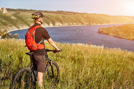 年轻骑自行车的人后视图站在大河上方的绿色草地上骑山地自行车图片