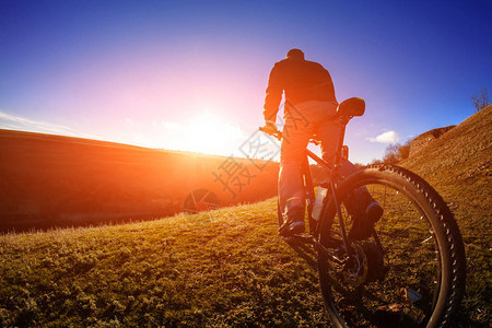 在日出时与阳光和蓝天空对立的山上自行车站立的骑手低角度视图闪烁季节极图片